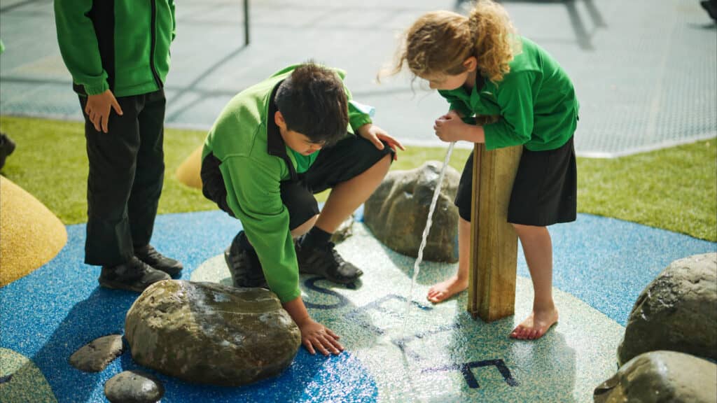 Children playing on water feature. Enhancing playground design and adds sensory play.